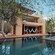 A pool in front of a 3-story pool house with tables and lounge chairs nearby